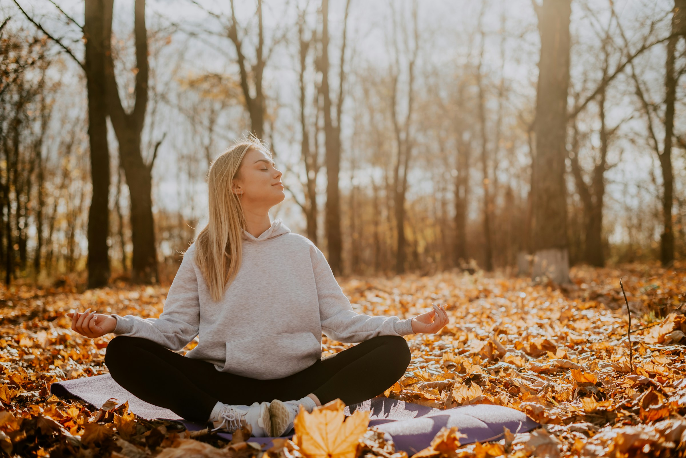 Woman meditating on a blanket in an autumn forest, image about current states, calm, and observing mood without judgment