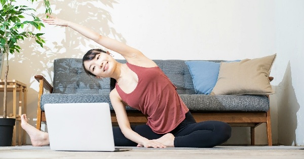 Woman doing a side stretch at home next to a laptop and sofa