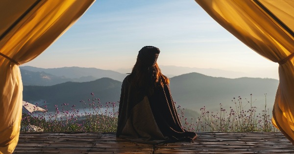 Person sitting at the entrance of a tent looking toward the mountains, representing perspective and creative ideas
