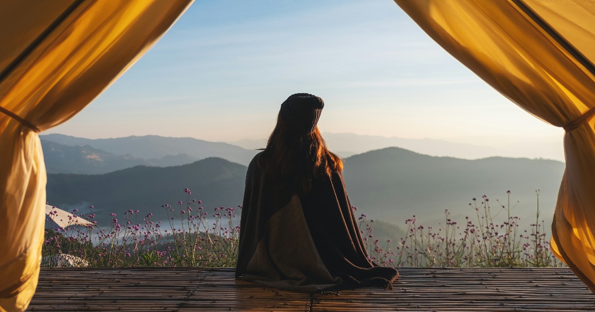 Person sitting at the entrance of a tent looking toward the mountains, representing perspective and creative ideas