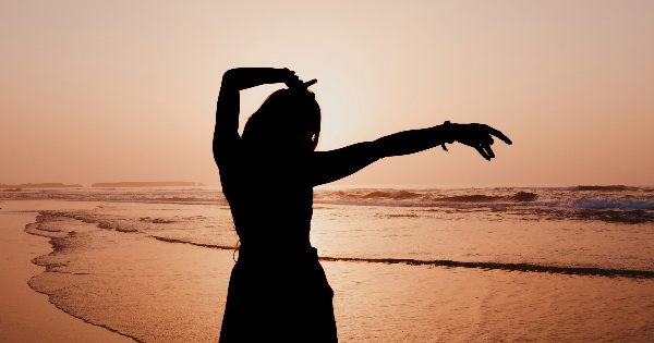 Silhouette of a woman on the beach at sunset with open arms, suggesting mental clarity and perspective