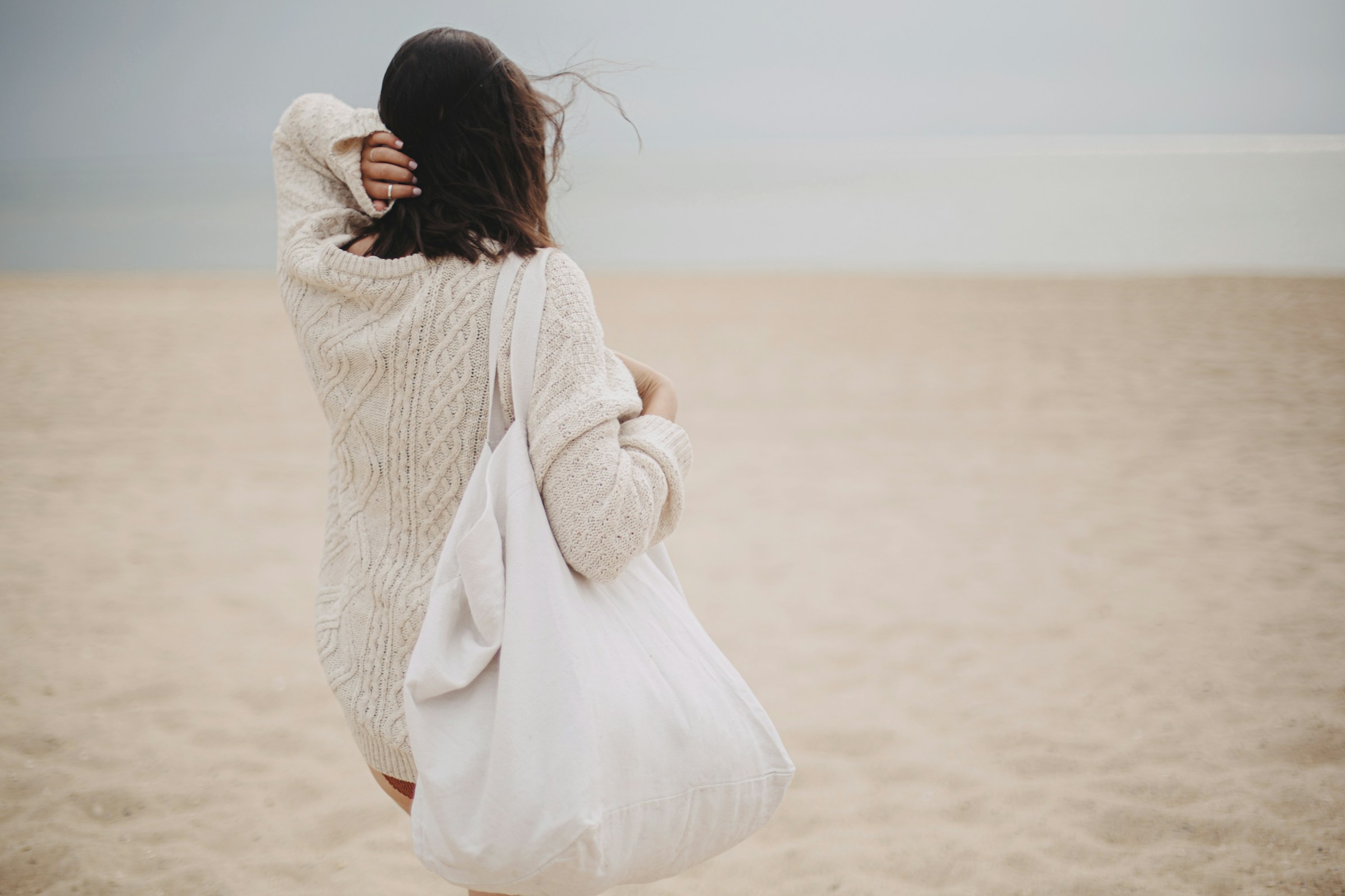 Woman seen from behind on an empty beach, image about identity, continuity, and an evolving personal story