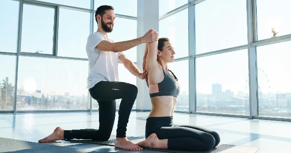 Instructor ajutand o femeie cu exercitiu de stretching yoga intr-un studio luminos