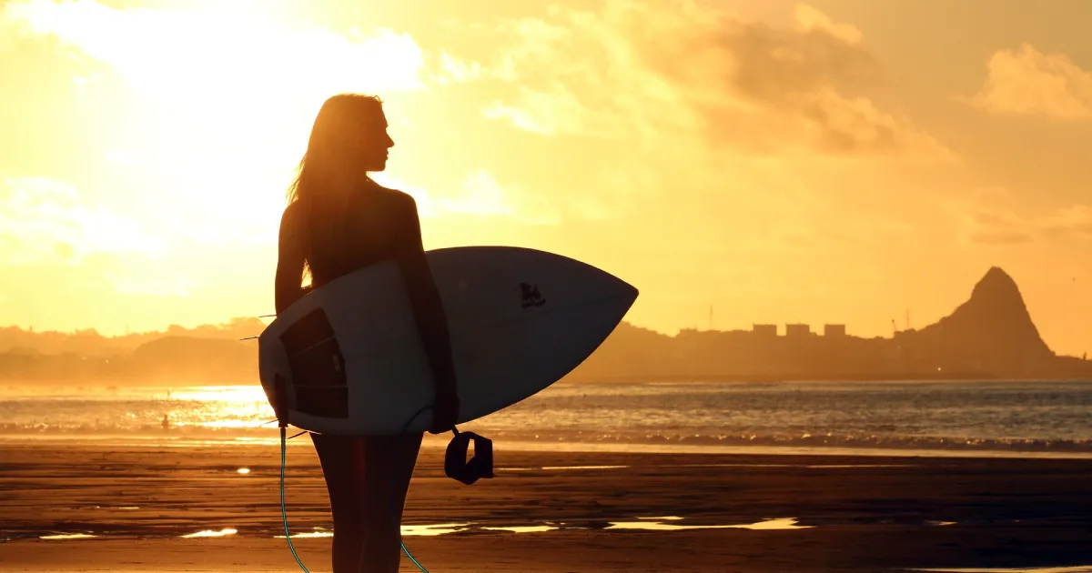 Siluetă de surfer pe plajă la apus, simbolizând motivația, energia, echilibrul și claritatea mentală.