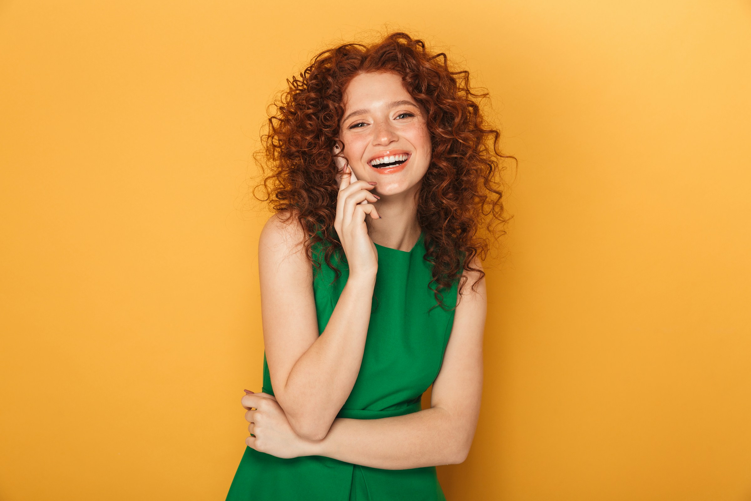 Smiling curly-haired woman on a warm orange background, image about personality traits, expression, and emotional style