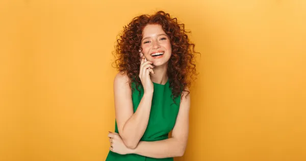Smiling curly-haired woman on a warm orange background, image about personality traits, expression, and emotional style